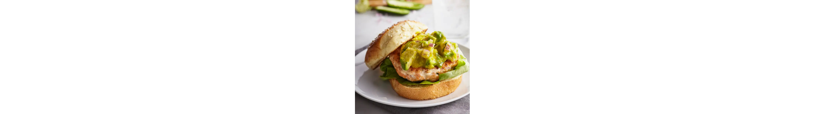Salmon burger topped with avocado on white plate