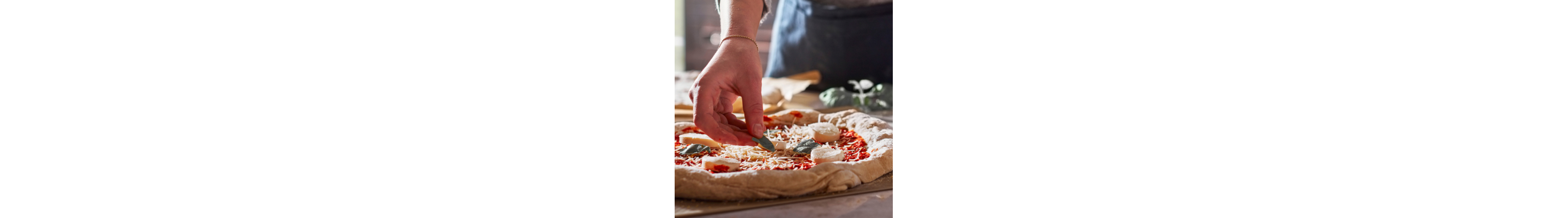 Maker adding ingredients to top of pizza