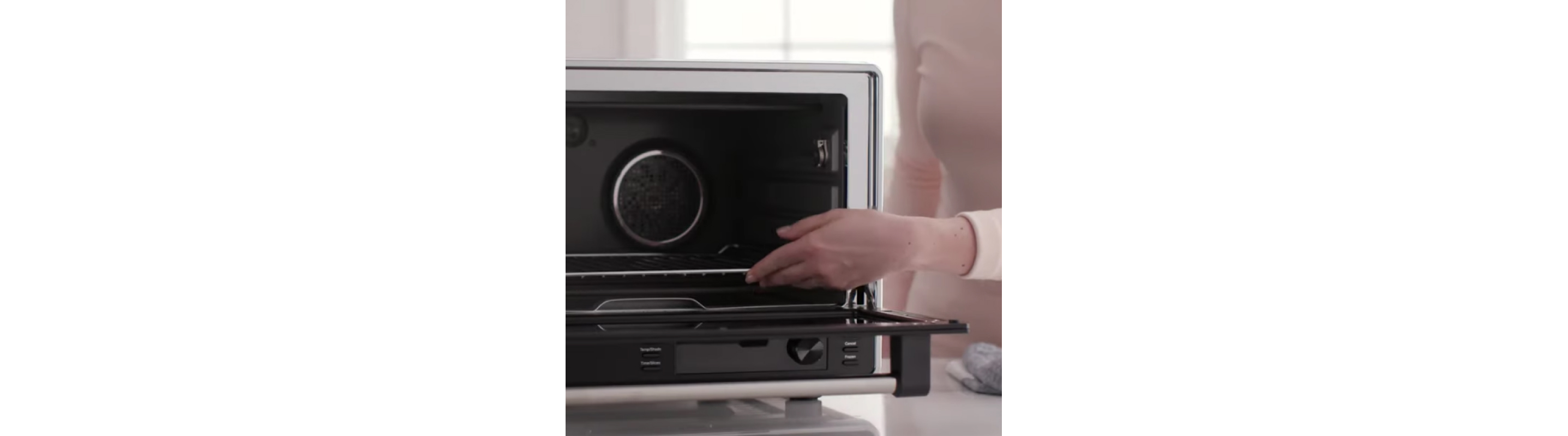 Person placing air fryer tray inside of black air fryer.