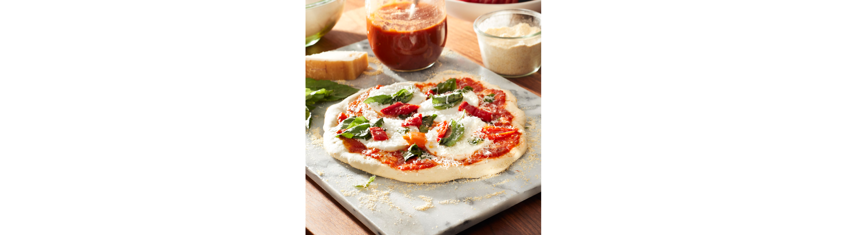 Homemade pizza on granite board surrounded by ingredients. 