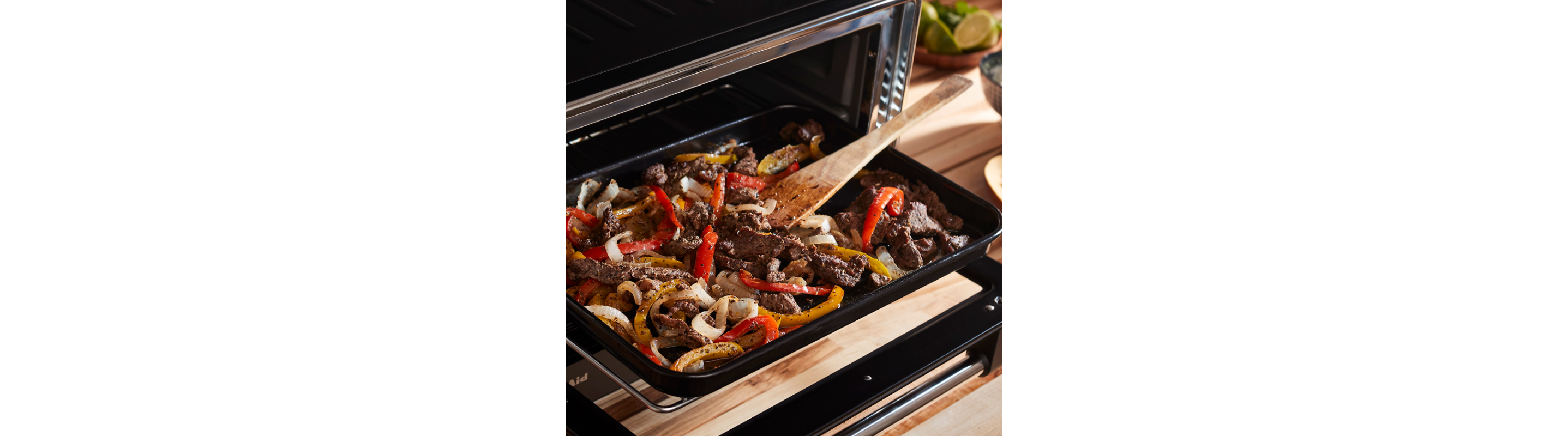 Meat and vegetables in tray of open air fryer with wooden spatula.