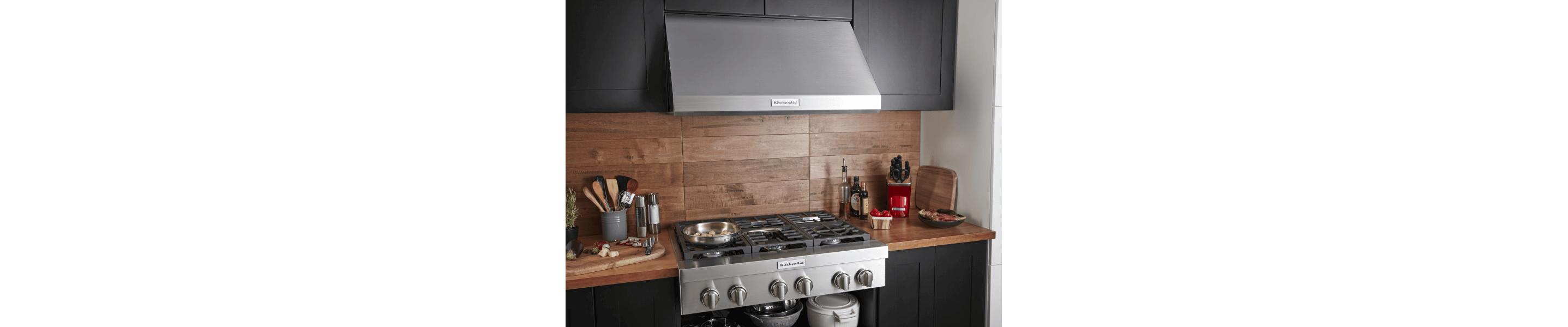 Stainless steel gas range and range hood set into a wooden countertop and backsplash