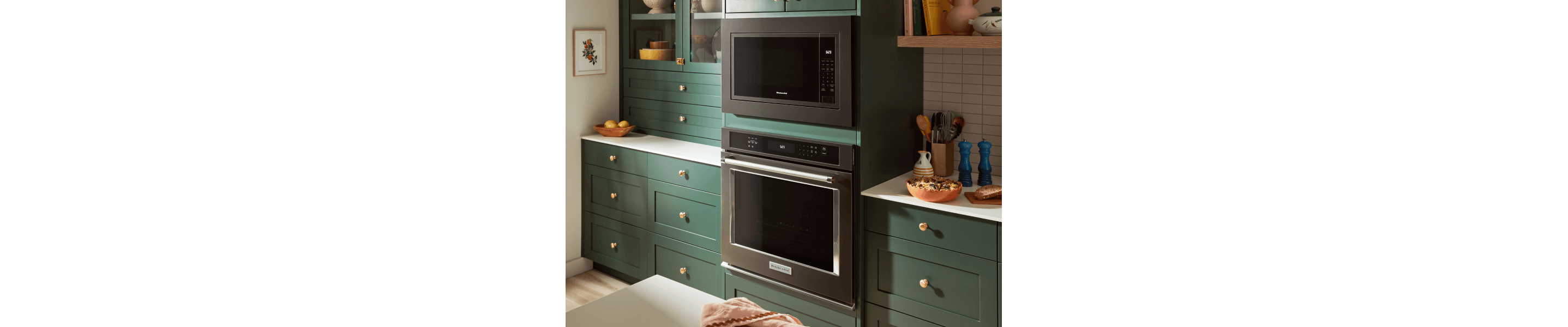 Stainless steel wall oven and black microwave set into deep green cabinetry