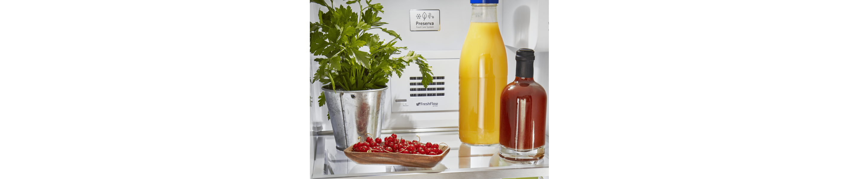 A jar of fresh orange juice and cherries on a refrigerator shelf.
