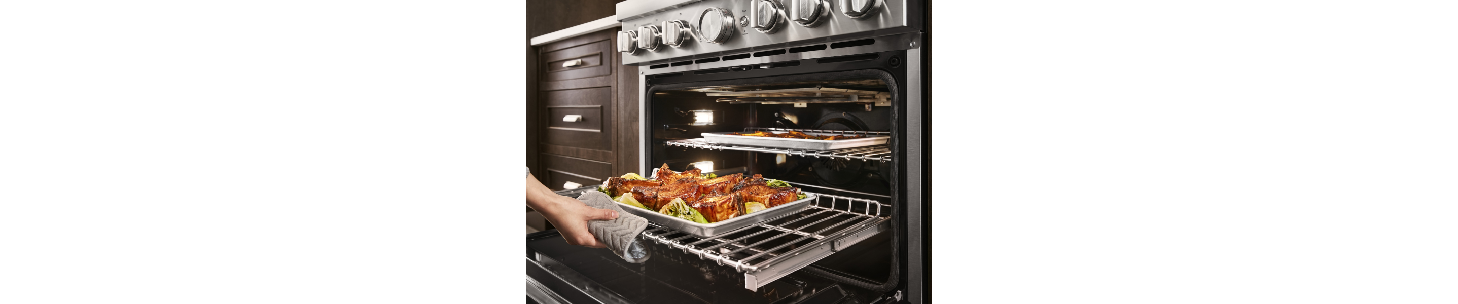 Person pulling a baking tray of roasted meat out of a KitchenAid® oven
