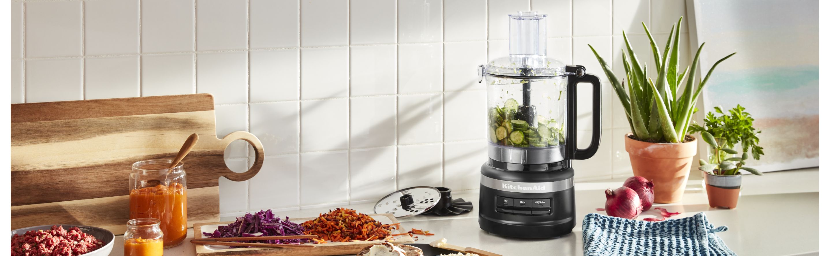 Sliced cucumbers in a KitchenAid® food processor next to shredded vegetables