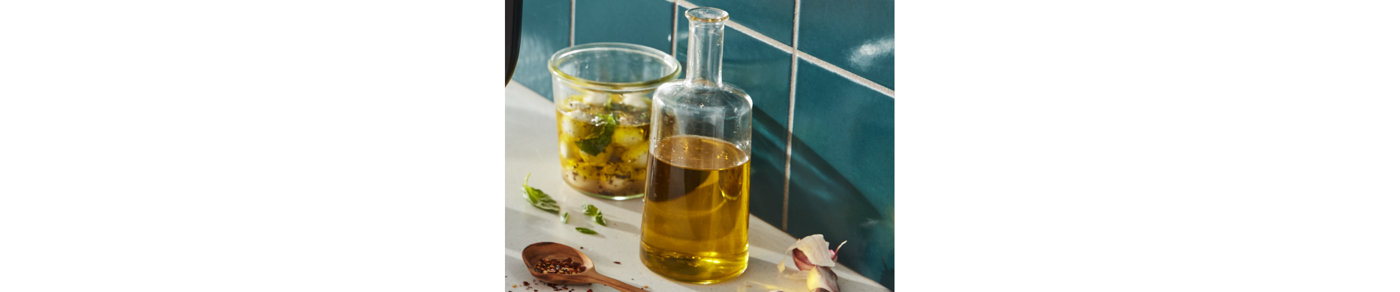 Bottle of olive oil next to a glass jar of marinated mozzarella 