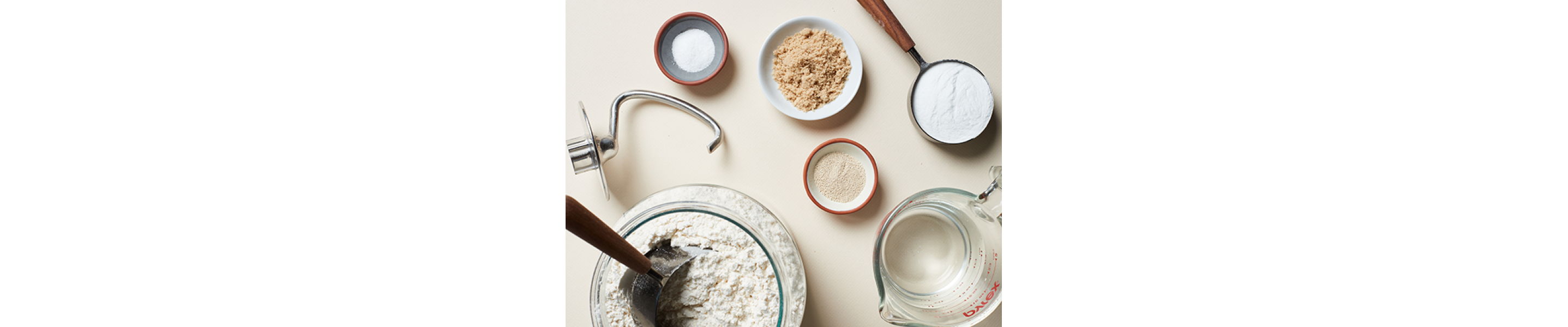 Various ingredients in bowls next to a dough hook accessory