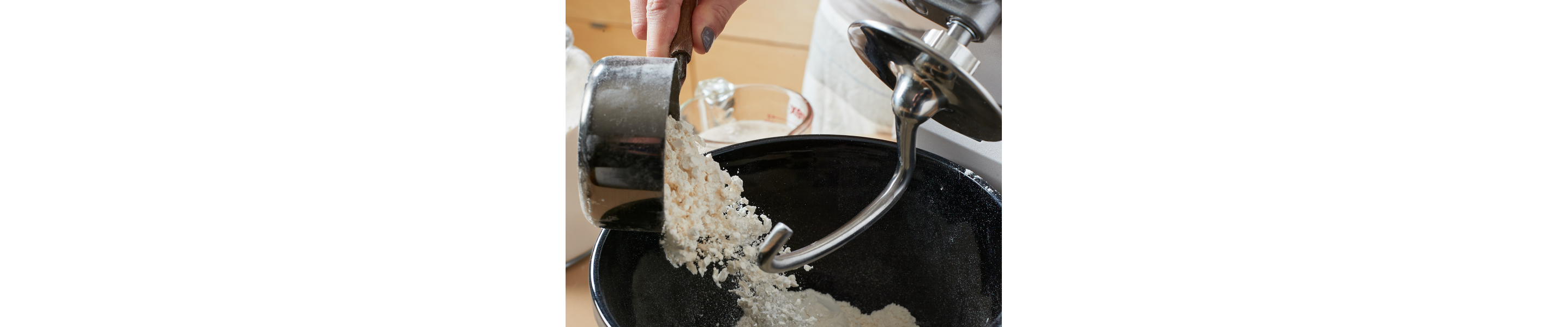 Person pouring flour into stand mixer equipped with a dough hook accessory