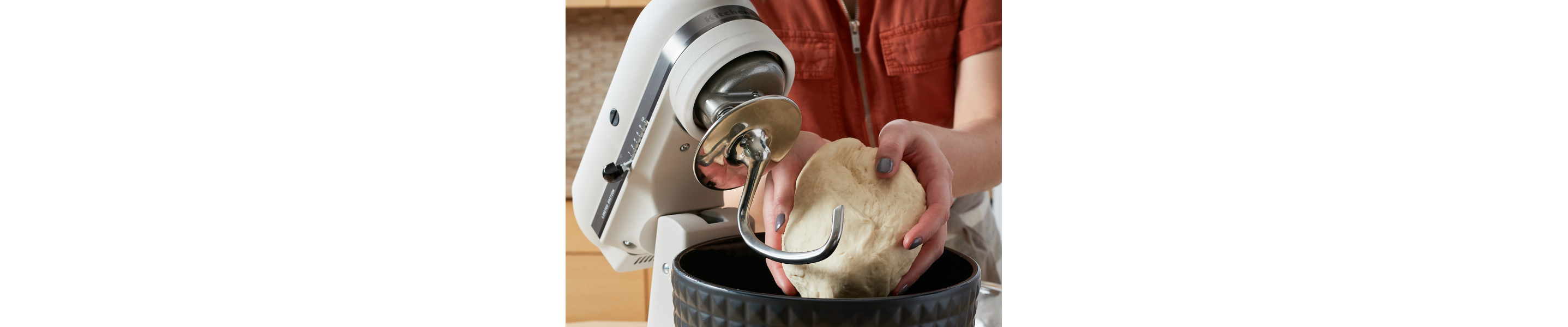 Person shaping ball of dough above black textured stand mixer bowl