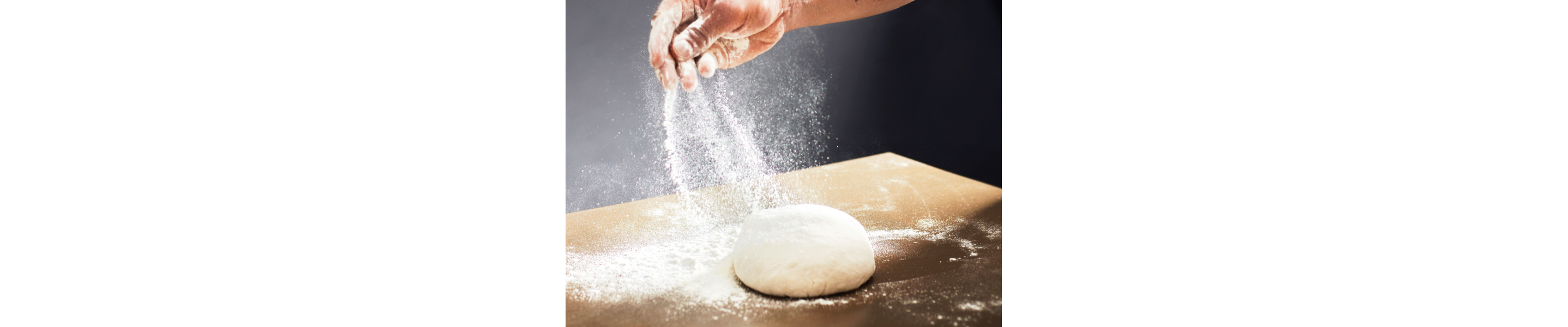 Person sprinkling flour on ball of dough sitting on a countertop