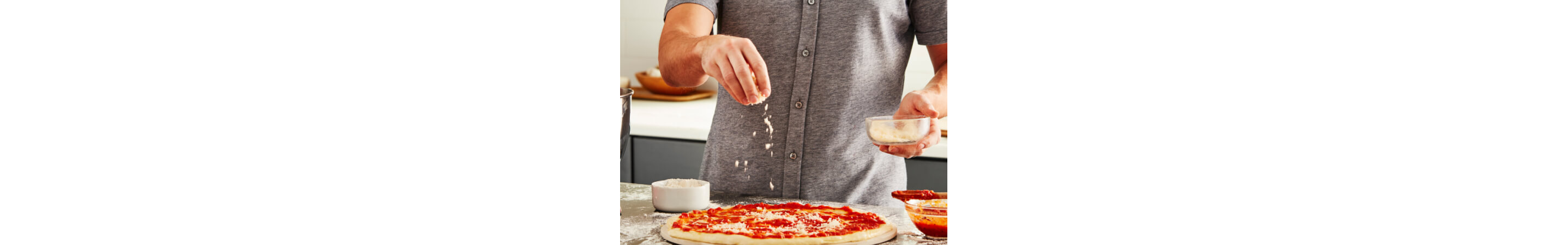 Person sprinkling cheese on a pizza
