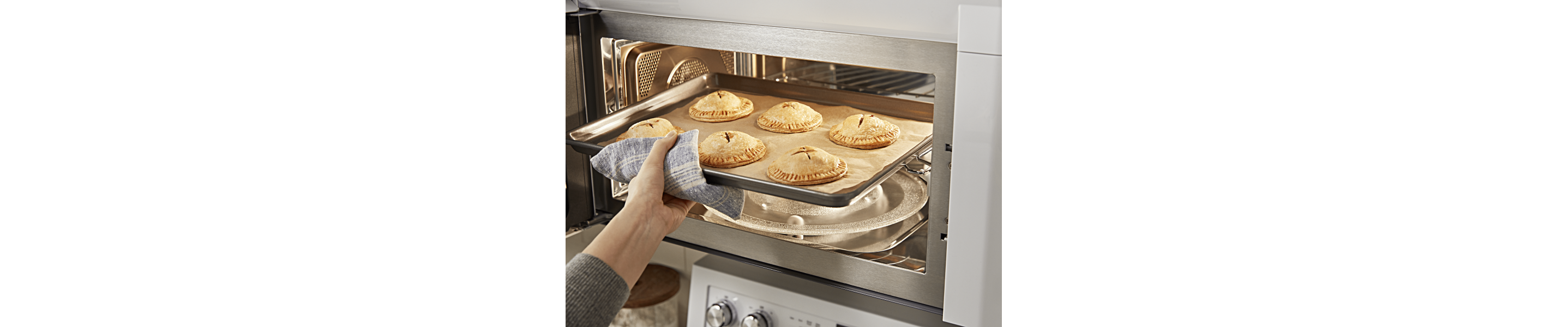 Person removing a tray of pastries from a convection microwave