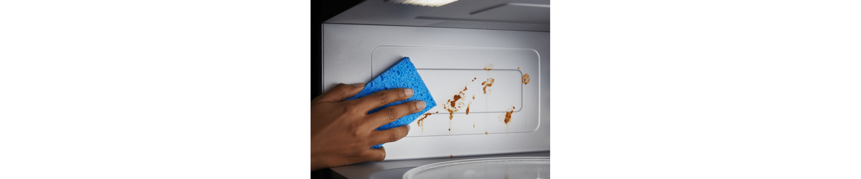 Person wiping down the inside of a microwave with a sponge