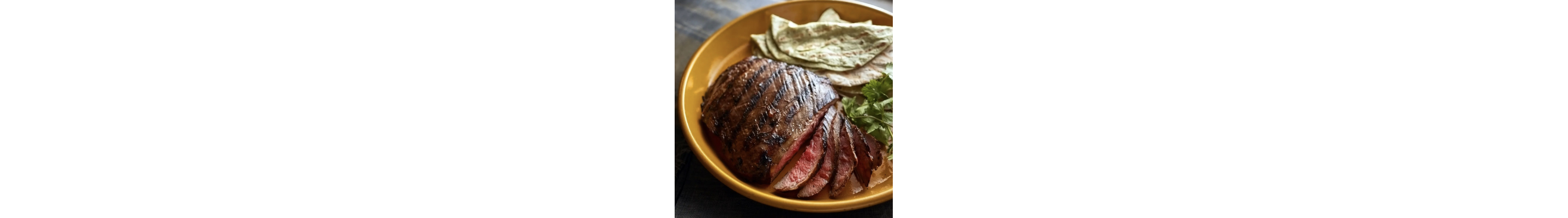 Sliced, grilled Tennessee steak on a plate with tortillas and herbs
