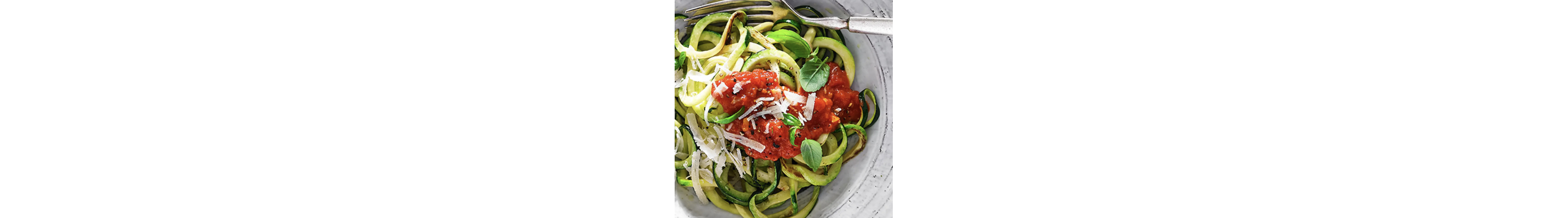 Zucchini noodles topped with grated cheese, red sauce and fresh herbs