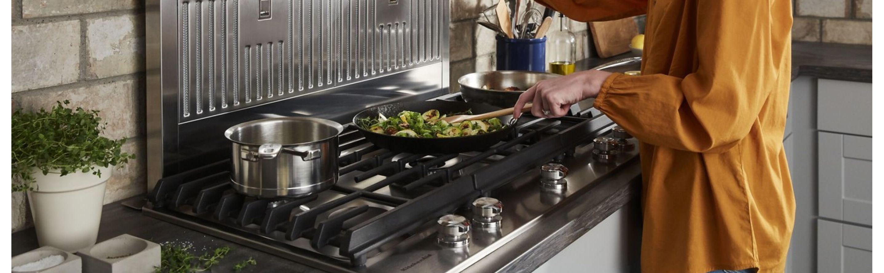 A closeup of a KitchenAid® gas cooktop with a person cooking food 
