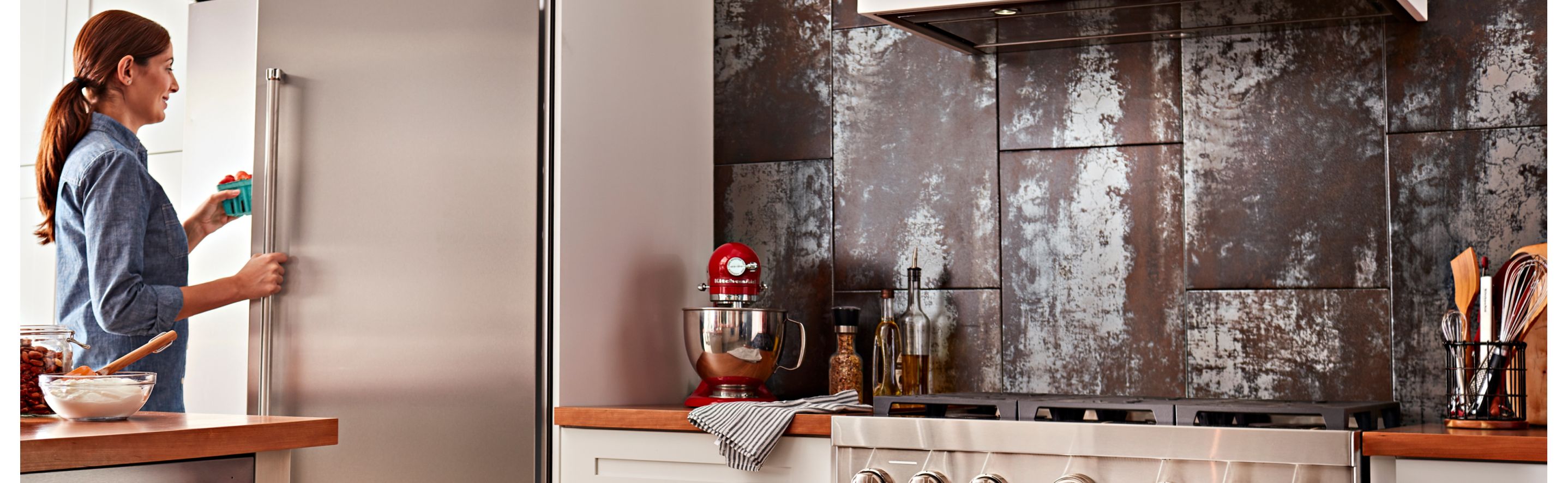 Woman opening a built-in side-by-side refrigerator in a kitchen with commercial-style appliances