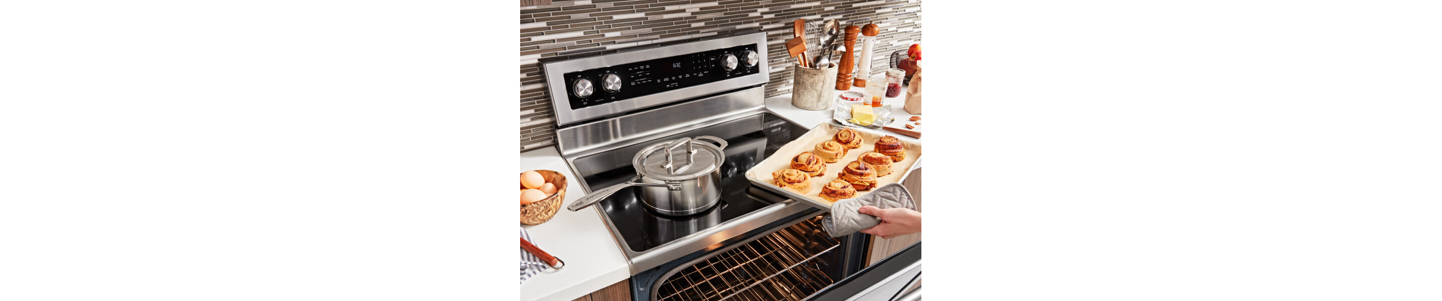 Person removing a tray of baked rolls from an electric range
