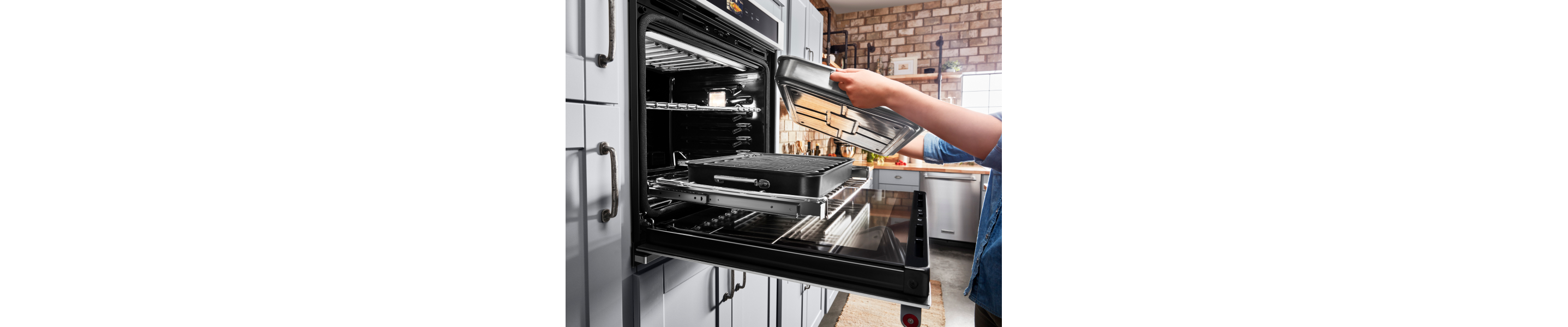A person placing a baking pan on the roll-out tray of a KitchenAid® Smart Oven+