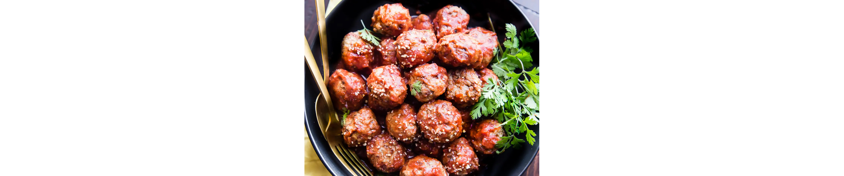 Birds-eye view of meatballs sprinkled with sesame seeds with cilantro on the side