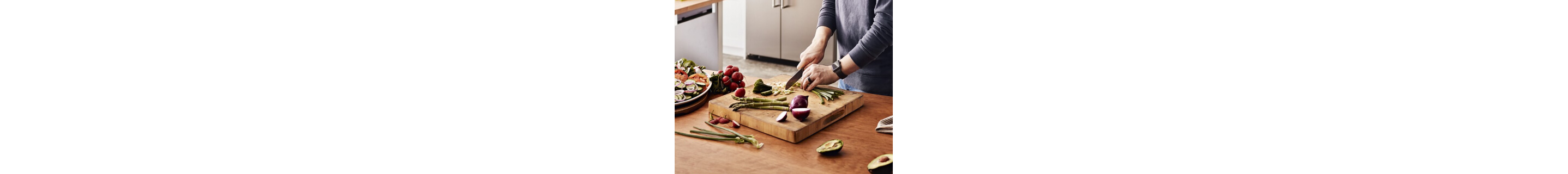 A person chopping onions, asparagus and other vegetables on a kitchen island