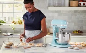A person spooning dough onto a tray next to a blue stand mixer