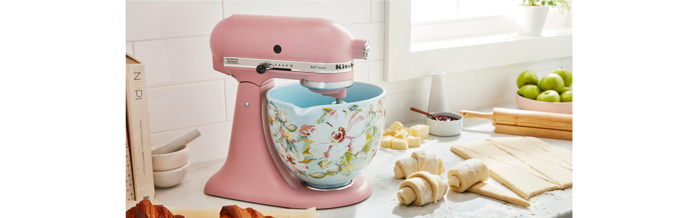 Pink stand mixer with a flower-covered bowl on a countertop next to dough for croissants