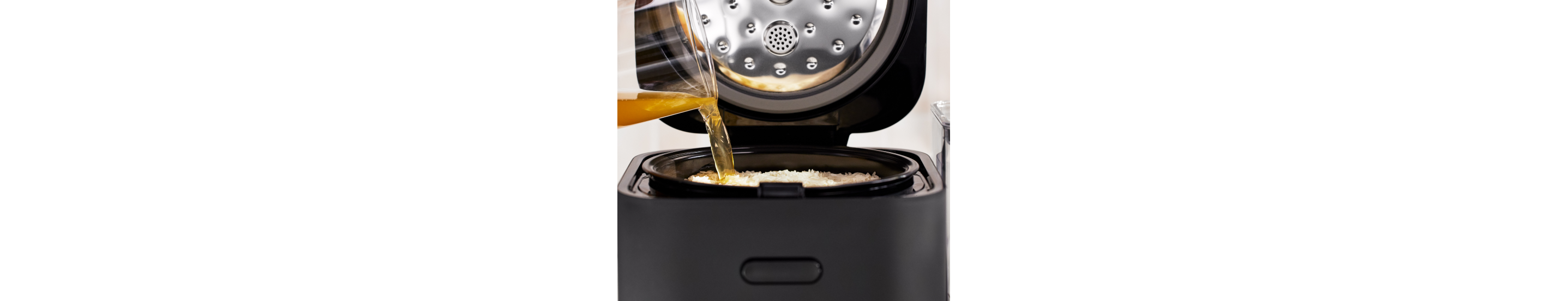 Broth being poured over uncooked white rice in the grain and rice cooker.