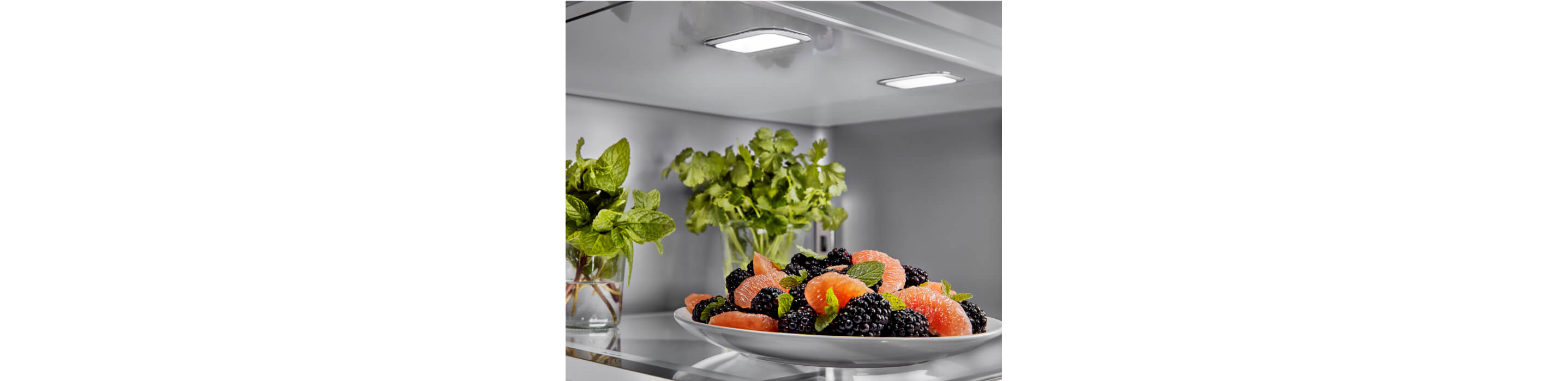 The top shelf of a KitchenAid® French Door Bottom Mount Refrigerator filled with fresh fruit and herbs.