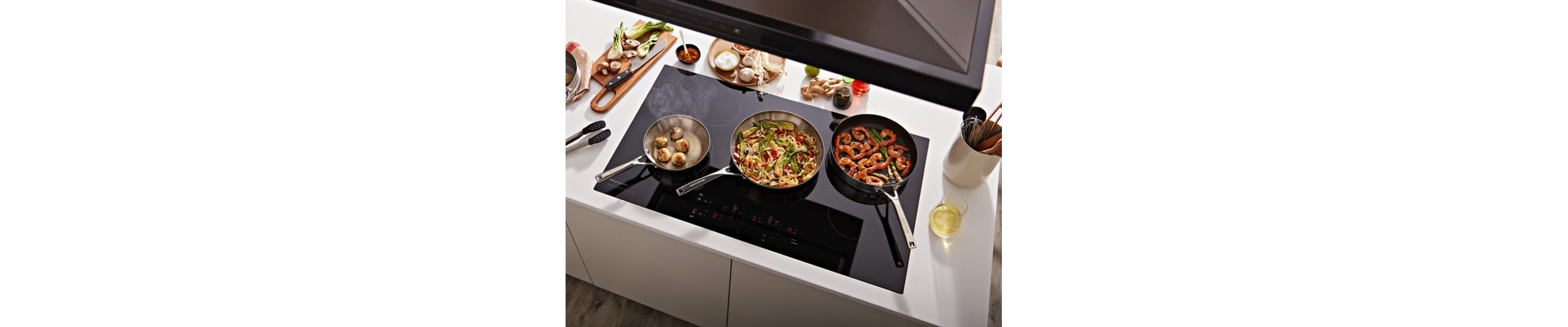 Three pans with food in them cooking on an induction cooktop